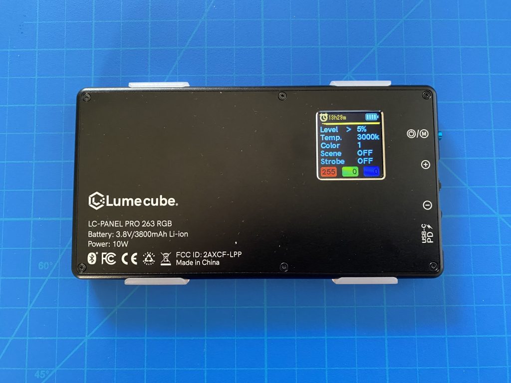 A LumeCube LC-Panel Pro LED light on a blue cutting mat, showing a detailed screen with battery life, time remaining (13h29m), brightness level (5%), color temperature (3000K), and other adjustable settings.