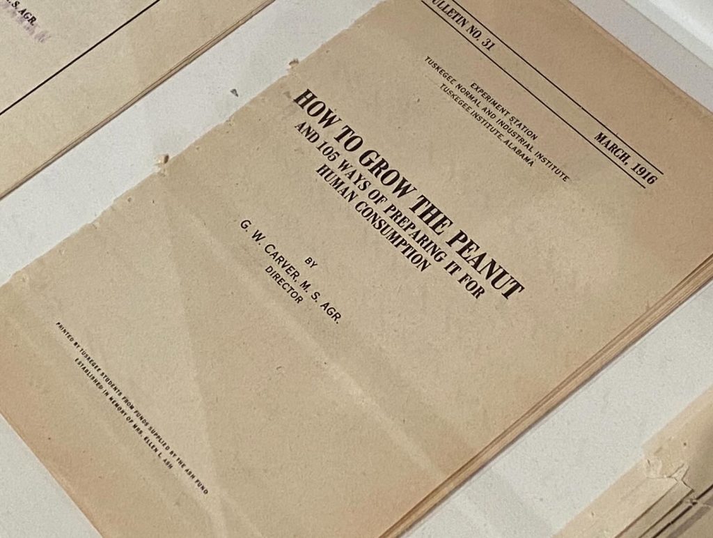 Close-up of a vintage agricultural bulletin titled “How to Grow the Peanut and 105 Ways of Preparing It for Human Consumption” by G.W. Carver, dated March 1916. The aged document lies flat under protective display, showing its Tuskegee Institute origins.